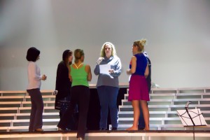 Heidi Jarret, facing out with paper in hand, working with the cast during the rehearsal.